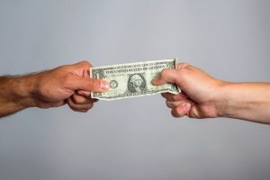 A man and a woman's hand pulling a dollar bill representing the financial conflicts that can prolong divorce proceedings.